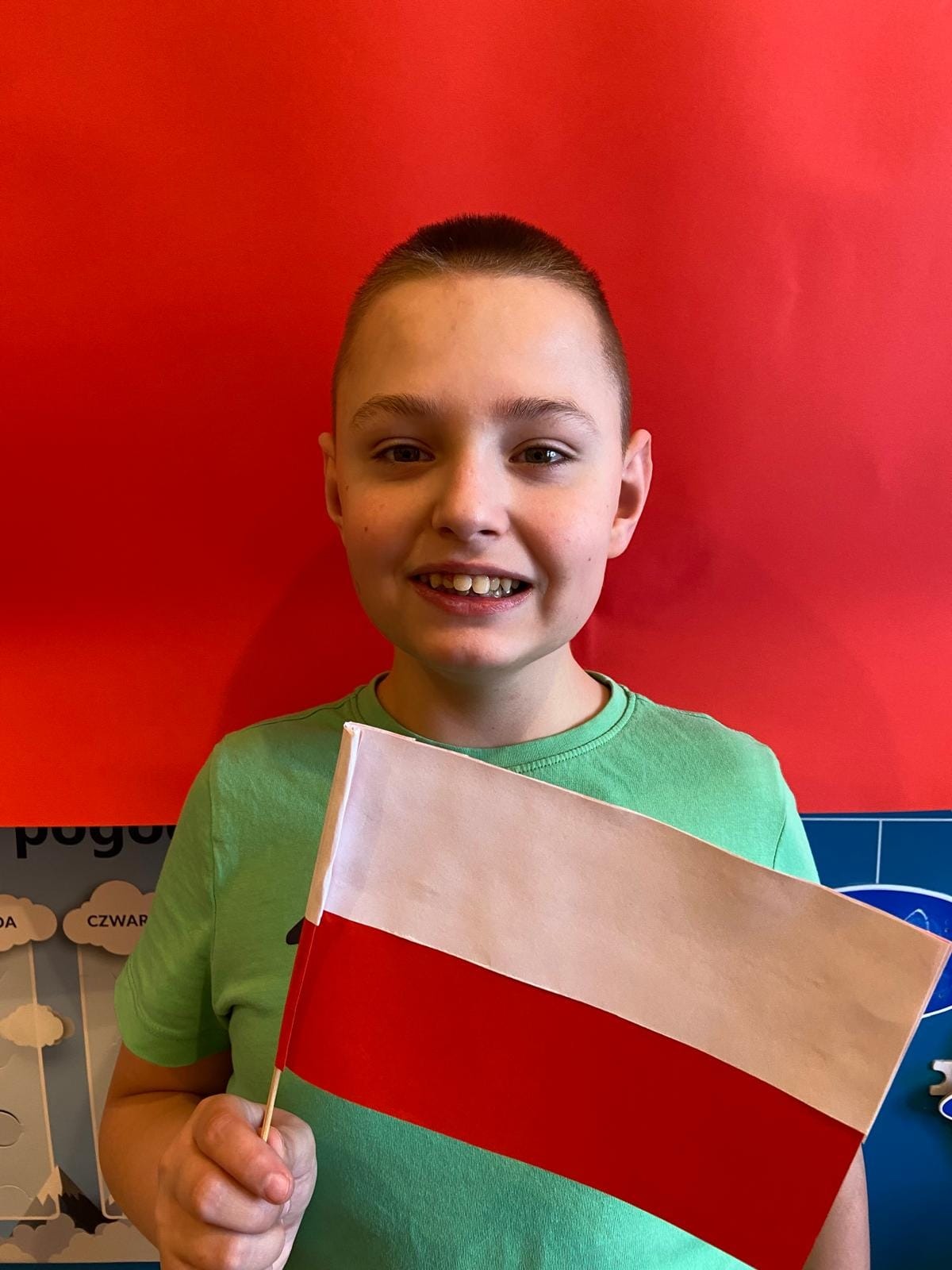 Uśmiechnięty uczeń trzyma w ręku flagę Polski