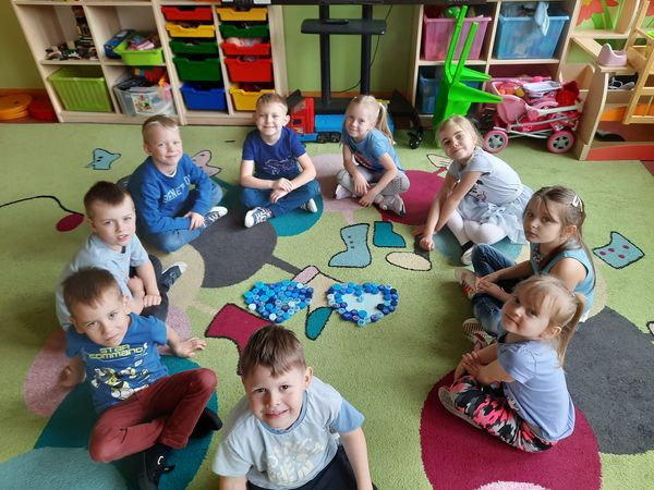 Dzieci  z oddziału przedszkolnego siedzą w kółeczku na dywanie. Każde z nich ma niebieski element stroju na znak solidarności z osobami z autyzmem. 