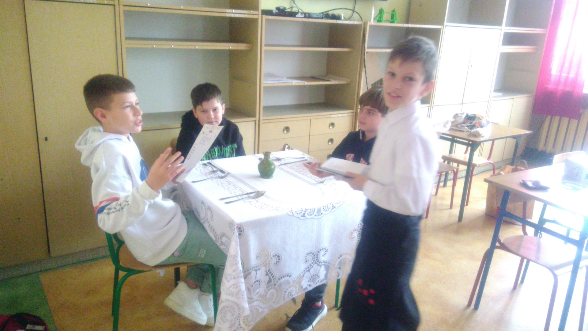 Zdjęcie 1: Uczniowie klasy 5b podczas zajęć innowacyjnych z języka angielskiego, prowadzonych przez Renatę Modras, odgrywający scenkę w restauracji.