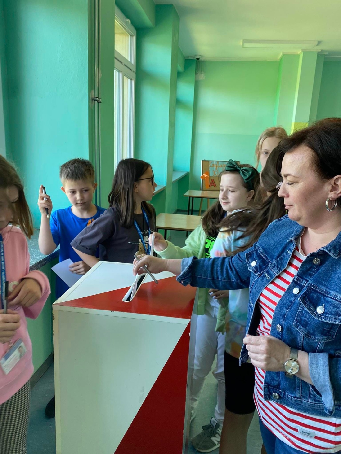 Nauczyciel i uczniowie wrzucają karty do głosowania do urny wyborczej.