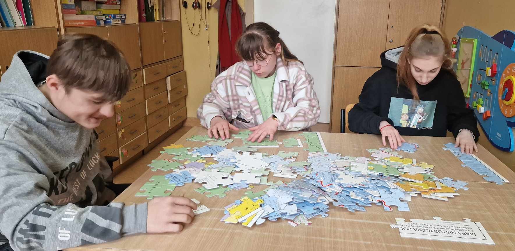 3 uczniów przy stoliku układa z puzzli mapę