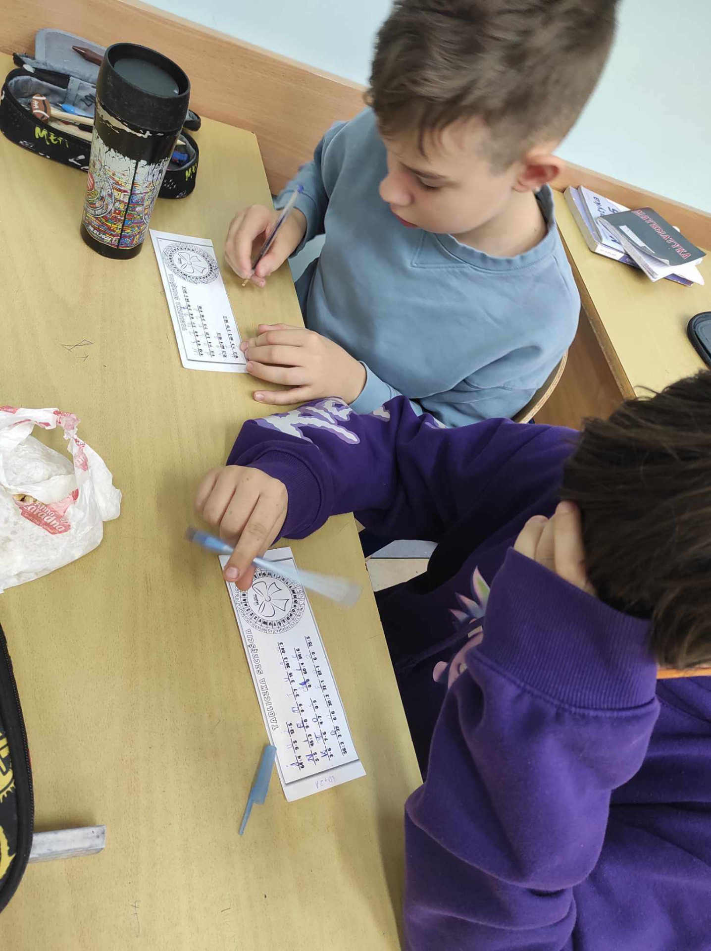 2 uczniów siedzi przy stoliku i rozwiązuje tabliczki szczęścia - rozwiazując przyklady z tabliczki mnożenia