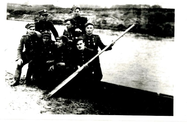 6 partyzantów w mundurach stoi na łodzi.