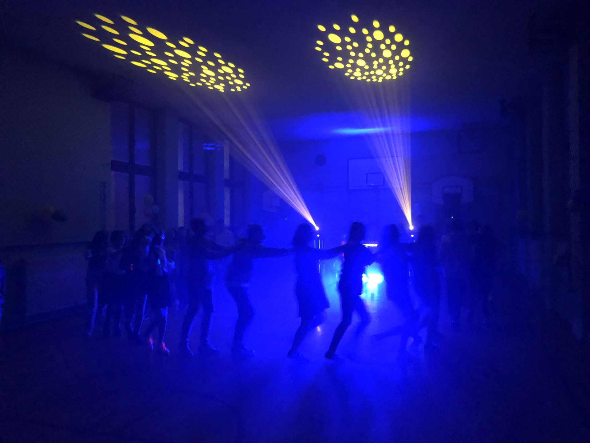 Uczniowie tańczący w sali gimnastycznej do muzyki puszczanej przez DJ