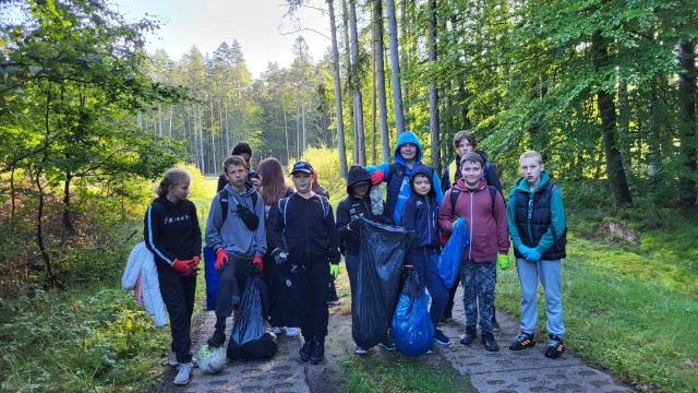 Uczniowie i nauczyciele sprzątający las.